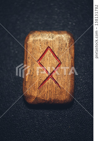 Vertical close-up of a handcrafted wooden Othala rune stone, featuring the carved ancestral symbol with red pigment. 138131782