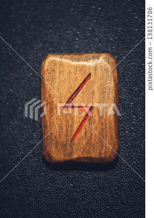 Vertical close-up of a handcrafted wooden Sowilo rune stone, featuring the carved sun symbol filled with red pigment on a rustic grain. Vertical close-up of a handcrafted wooden Sowilo rune stone, featuring the carved sun symbol filled with red pigment on a rustic grain. 138131786