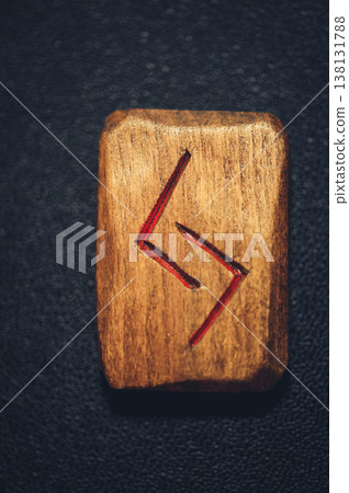 Vertical close-up of a handcrafted wooden Jera rune stone, featuring the carved two-part harvest symbol filled with red pigment. 138131788