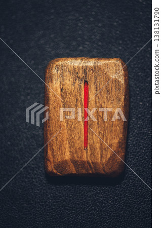 Vertical close-up of a handcrafted wooden Isa rune stone, with the single vertical ice symbol carved and filled with red pigment on a rustic grain. Vertical close-up of a handcrafted wooden Isa rune stone, with the single vertical ice symbol carved and filled with red pigment on a rustic grain. 138131790