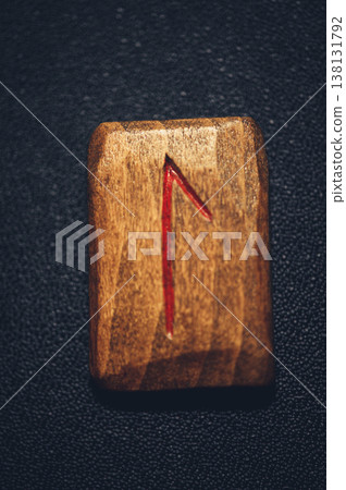 Vertical close-up of a handcrafted wooden Laguz rune stone, featuring the carved water symbol filled with red pigment on a rustic grain. Vertical close-up of a handcrafted wooden Laguz rune stone, featuring the carved water symbol filled with red pigment on a rustic grain. 138131792