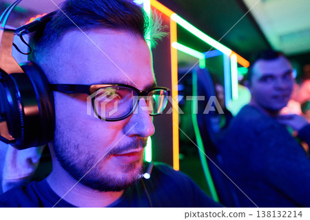 Focused Gamer Wearing Headset in Neon-Lit Esports Arena With Team and Gaming Stations Focused Gamer Wearing Headset in Neon-Lit Esports Arena With Team and Gaming Stations 138132214