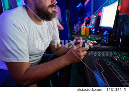 Bearded Man Playing Video Games With Controller at Neon-Lit PC Gaming Setup in Arcade Bearded Man Playing Video Games With Controller at Neon-Lit PC Gaming Setup in Arcade 138132245