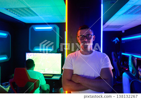 Confident Gamer Standing in Neon Esports Gaming Room With Team Competing at Monitors Confident Gamer Standing in Neon Esports Gaming Room With Team Competing at Monitors 138132267