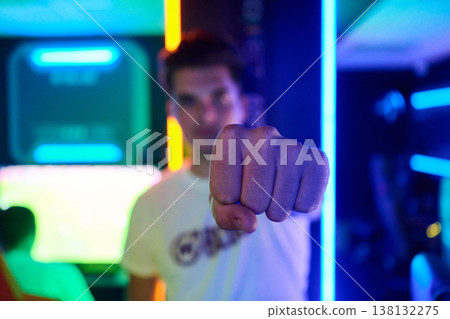 Young Gamer Punching Fist Toward Camera in Neon Arcade With Confident Gesture and Vivid Lighting Young Gamer Punching Fist Toward Camera in Neon Arcade With Confident Gesture and Vivid Lighting 138132275