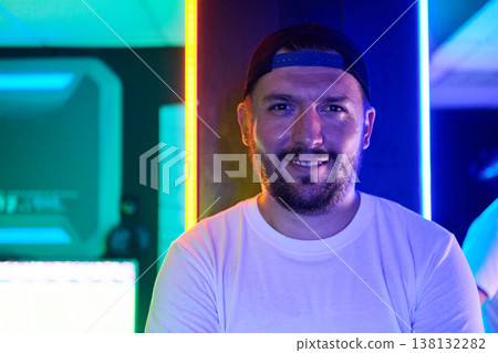 Smiling Man Portrait in Neon Light Wearing Cap and White T-Shirt in Modern Arcade Smiling Man Portrait in Neon Light Wearing Cap and White T-Shirt in Modern Arcade 138132282