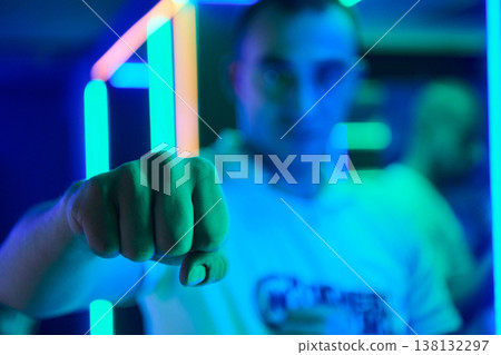 Young Man Showing Fist Toward Camera in Neon Blue Nightclub With Colorful LED Lights Young Man Showing Fist Toward Camera in Neon Blue Nightclub With Colorful LED Lights 138132297