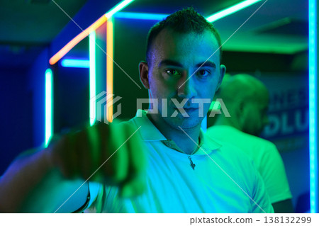 Confident Young Man Pointing Toward Camera in Neon-Lit Nightclub Portrait With Futuristic Lighting Confident Young Man Pointing Toward Camera in Neon-Lit Nightclub Portrait With Futuristic Lighting 138132299