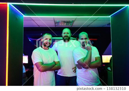 Three Male Gamers Standing Together in Neon-Lit Gaming Room Showing Team Spirit and Confidence 138132310