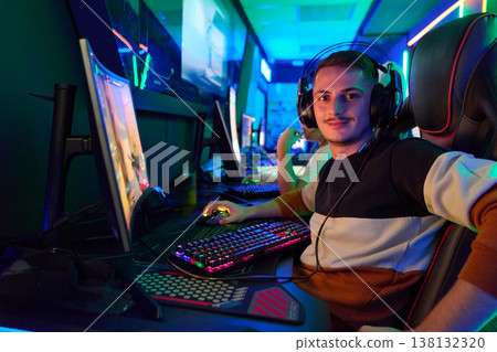 Young Gamer Wearing Headset in Neon-Lit Gaming Center Playing Multiplayer PC Games With Teammates Young Gamer Wearing Headset in Neon-Lit Gaming Center Playing Multiplayer PC Games With Teammates 138132320