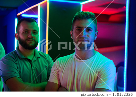 Two Young Men Standing Confidently in Neon-Lit Arcade Portrait With Colorful LED Lights 138132326
