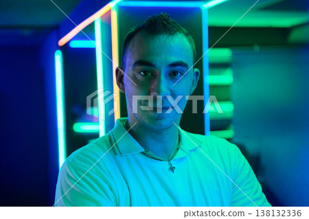 Confident Young Man Neon Portrait in Blue Green Light at Nightclub or Gaming Lounge Confident Young Man Neon Portrait in Blue Green Light at Nightclub or Gaming Lounge 138132336