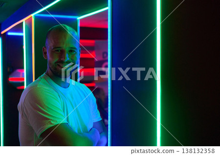 Smiling Man Standing in Neon LED Light Corridor at Nightclub With Colorful Ambient Lighting Smiling Man Standing in Neon LED Light Corridor at Nightclub With Colorful Ambient Lighting 138132358
