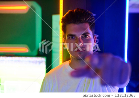 Young Man Pointing at Camera in Neon Gaming Room With LED Lights and Confident Expression Young Man Pointing at Camera in Neon Gaming Room With LED Lights and Confident Expression 138132363