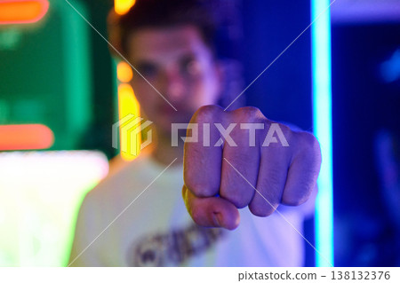 Young Man Punching Forward With Neon Lights In Nightclub Showing Confidence And Power Young Man Punching Forward With Neon Lights In Nightclub Showing Confidence And Power 138132376