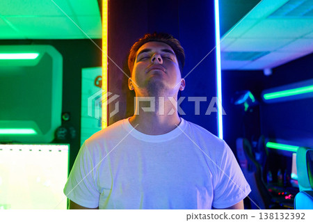 Young Gamer Relaxing Against Neon Pillar in LED-Lit Gaming Room With Cyberpunk Mood Young Gamer Relaxing Against Neon Pillar in LED-Lit Gaming Room With Cyberpunk Mood 138132392