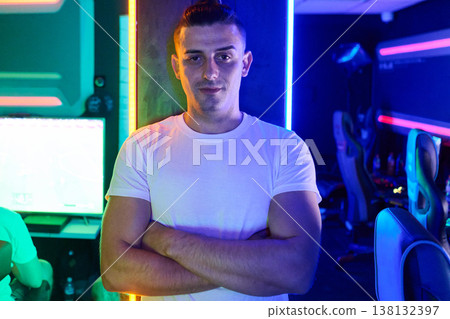Confident Gamer Standing With Arms Crossed in Neon Esports Gaming Room Confident Gamer Standing With Arms Crossed in Neon Esports Gaming Room 138132397