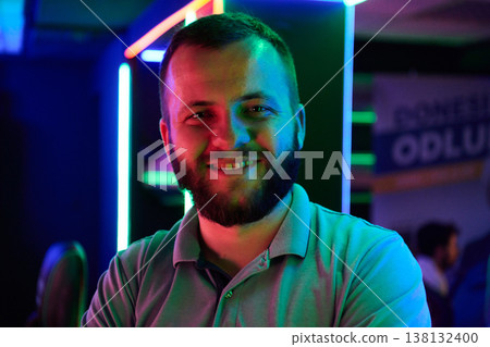 Smiling Bearded Man Portrait in Neon Lights at Nightclub or Gaming Lounge Smiling Bearded Man Portrait in Neon Lights at Nightclub or Gaming Lounge 138132400
