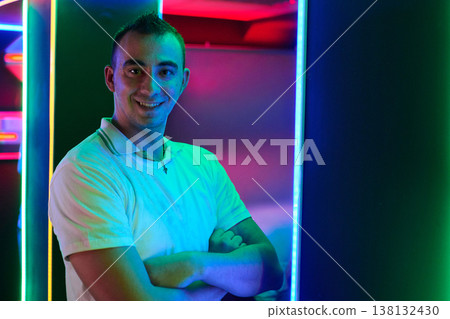 Smiling Young Man in White Polo Shirt Posing Under Vibrant Neon Lights Smiling Young Man in White Polo Shirt Posing Under Vibrant Neon Lights 138132430