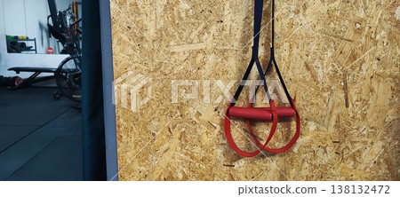 Suspension training straps hanging on a gym wall with fitness equipment in the background. Concepts of functional training, fitness lifestyle, and modern workout routines. Suspension training straps hanging on a gym wall with fitness equipment in the background. Concepts of functional training, fitness lifestyle, and modern workout routines. 138132472