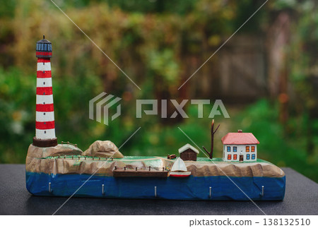 Horizontal eye-level view of a handcrafted wooden key holder with a detailed miniature seaside diorama, featuring a lighthouse and small houses. Horizontal eye-level view of a handcrafted wooden key holder with a detailed miniature seaside diorama, featuring a lighthouse and small houses. 138132510