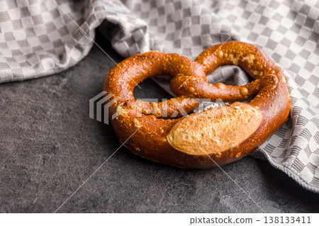 Traditional Soft Pretzel With Coarse Salt On Dark Stone Surface Beside Kitchen Towel 138133411