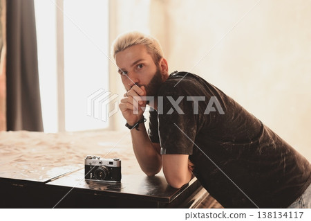 Pensive Caucasian man leaning on desk with old film camera Pensive Caucasian man leaning on desk with old film camera 138134117