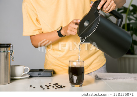 Man making use kettle pouring hot water making iced coffee or cold americano coffee into the cup with equipment, tool digital scale on the wooden bar at kitchen home Man making use kettle pouring hot water making iced coffee or cold americano coffee into the cup with equipment, tool digital scale on the wooden bar at kitchen home 138136071