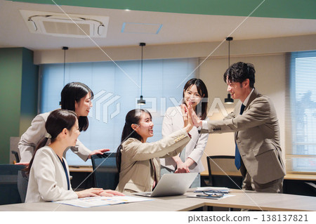 一位女士欣喜若狂，在辦公室與其他人擊掌慶祝。 138137821