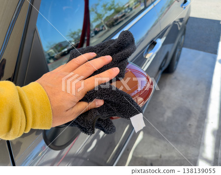 Man wiping and drying car with grey microfiber rag outdoors, closeup 138139055