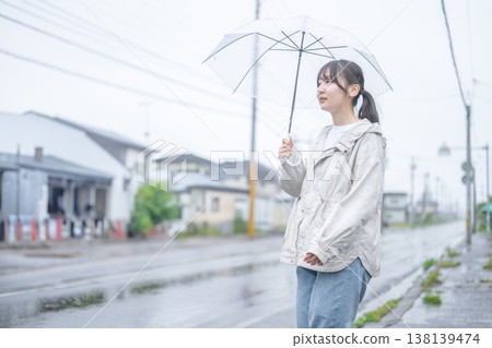 一位年輕女子撐著傘站在雨中的城市。 一位年輕女子撐著傘站在雨中的城市。 138139474