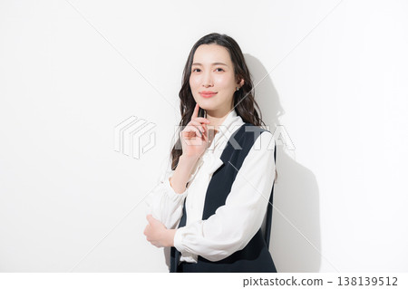一位留著黑色長髮的時尚女性，身穿商務休閒裝，包括一件長版背心，雙臂交叉抱在胸前。 138139512