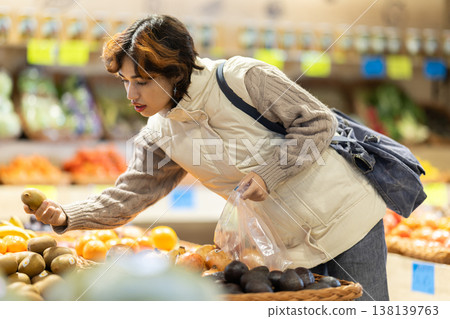 Girl near vegetable stand in store choose mango. Girl near vegetable stand in store choose mango. 138139763