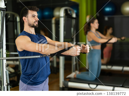 Young man training arms and shoulders on pilates reformer Young man training arms and shoulders on pilates reformer 138139772