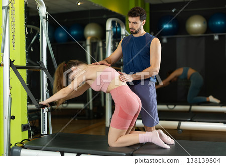 Male trainer guiding girl performing spine stretch on pilates reformer 138139804