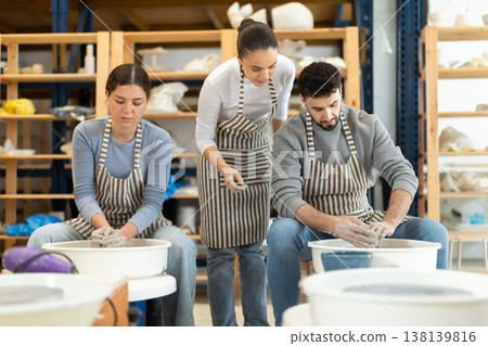 Female teacher help man sculpting ceramic product from clay on pottery wheel in workshop 138139816