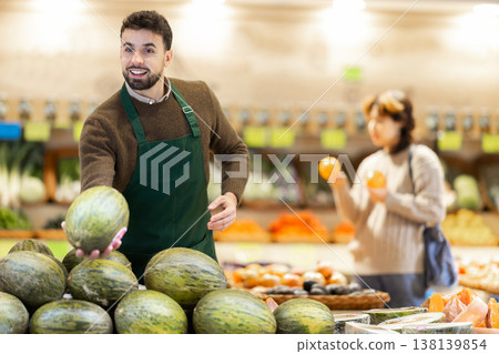 Man seller in grocery vegetable shop arrange melon. Man seller in grocery vegetable shop arrange melon. 138139854