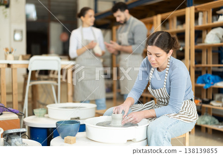 Woman in ceramics workshop with pottery wheel and various clay vessels 138139855