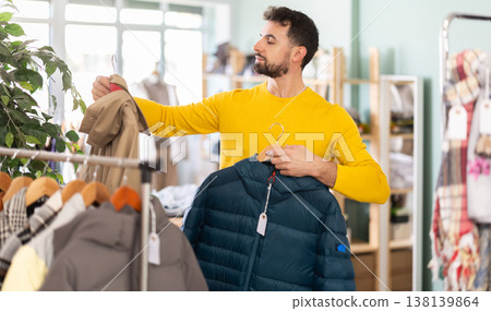 Young man choosing down jacket in clothing store Young man choosing down jacket in clothing store 138139864