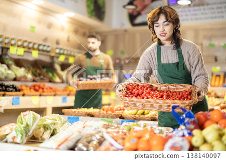 Young woman seller puts tomatoes in store Young woman seller puts tomatoes in store 138140097