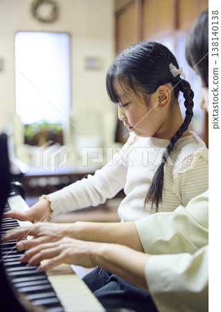 A senior piano teacher and her student girl giving a lesson at a piano studio. A senior piano teacher and her student girl giving a lesson at a piano studio. 138140138