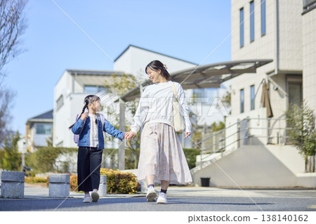 一位母親和她背著書包的女兒手牽手走過住宅區。 一位母親和她背著書包的女兒手牽手走過住宅區。 138140162