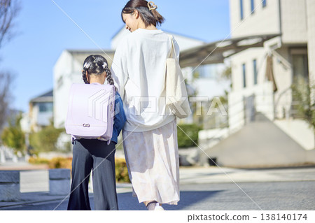 一位母親走過居民區,背對著背著書包的女兒。 一位母親走過居民區,背對著背著書包的女兒。 138140174