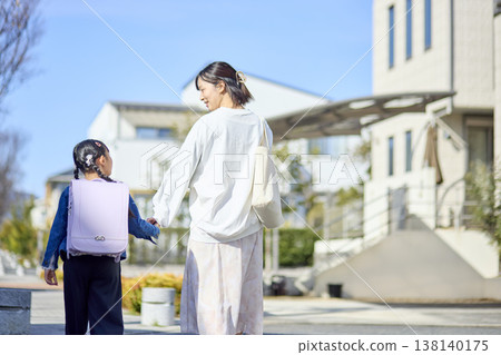 一位小學生和她的母親在上學路上互相看著對方，手牽手。 138140175