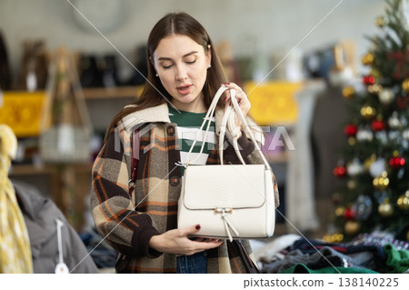 adult woman chooses fashionable handbags in a store against the background of a Christmas tree adult woman chooses fashionable handbags in a store against the background of a Christmas tree 138140225