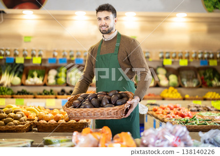 Male employees in uniform carries a wicker basket with avocado in grocery shop Male employees in uniform carries a wicker basket with avocado in grocery shop 138140226