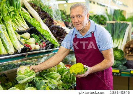 Aged salesman putting cauliflower on food stall in greengrocery Aged salesman putting cauliflower on food stall in greengrocery 138140246