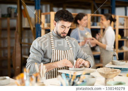 Guy sitting at table, busy making products from raw clay Guy sitting at table, busy making products from raw clay 138140279