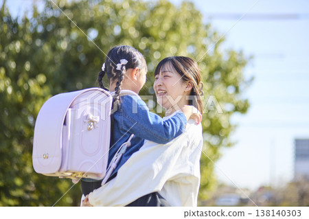 A mother laughs as she picks up her new student, still wearing her schoolbag. 138140303