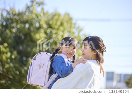A little girl in a school backpack smiles at the camera while being held by her mother. A little girl in a school backpack smiles at the camera while being held by her mother. 138140304